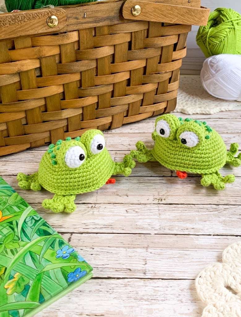 Two finished tiny green crochet frogs beside yarn, shown in the original pattern cover photo.