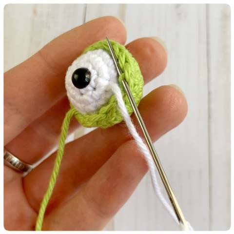 Original crochet frog tutorial photo 28, showing the eyes being assembled and sewn onto the frog.