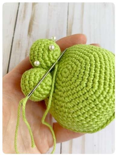 Original crochet frog tutorial photo 36, showing the eyes being assembled and sewn onto the frog.