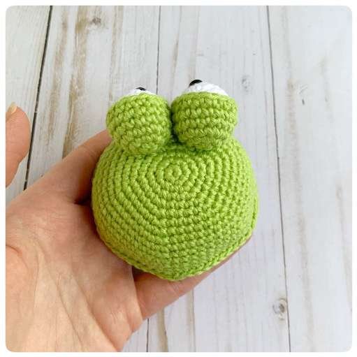 Original crochet frog tutorial photo 38, showing the eyes being assembled and sewn onto the frog.