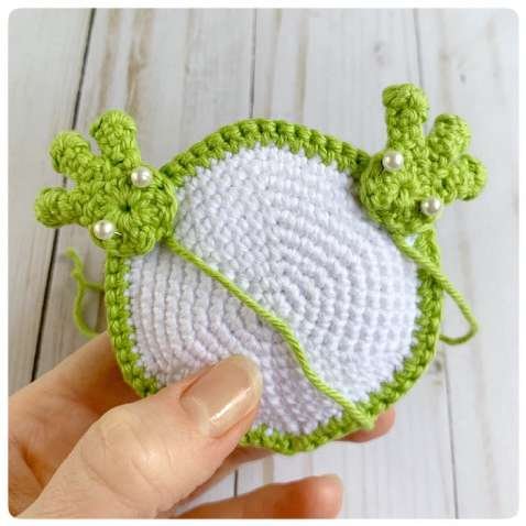 Original crochet frog tutorial photo 39, showing the front paws being positioned and sewn on.