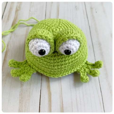 Original crochet frog tutorial photo 40, showing the front paws being positioned and sewn on.