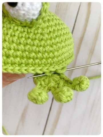 Original crochet frog tutorial photo 42, showing the front paws being positioned and sewn on.