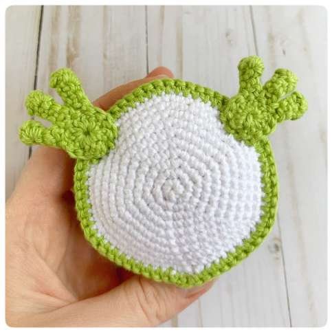 Original crochet frog tutorial photo 44, showing the front paws being positioned and sewn on.
