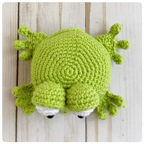 Original crochet frog tutorial photo 46, showing the back paws being positioned and sewn on.
