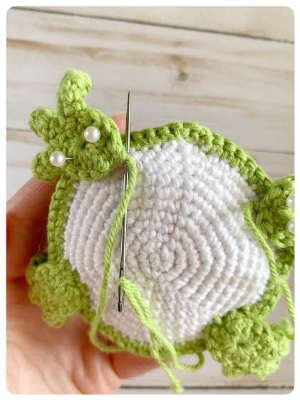 Original crochet frog tutorial photo 47, showing the back paws being positioned and sewn on.