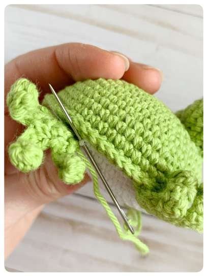 Original crochet frog tutorial photo 49, showing the back paws being positioned and sewn on.