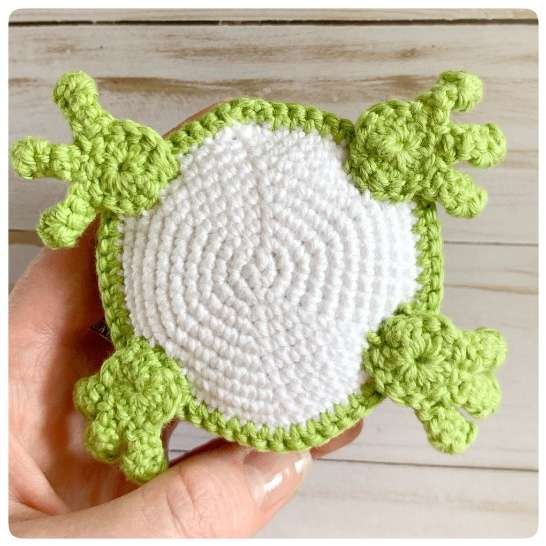 Original crochet frog tutorial photo 50, showing the back paws being positioned and sewn on.